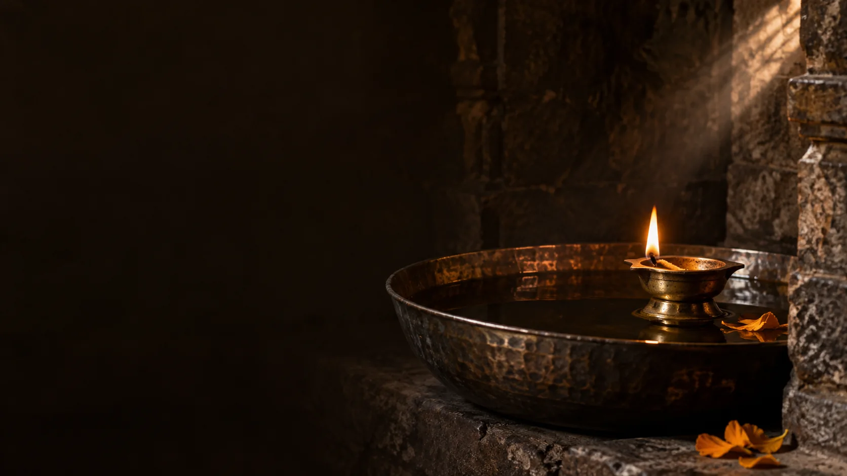 A brass diya and its reflection in still water in a temple niche